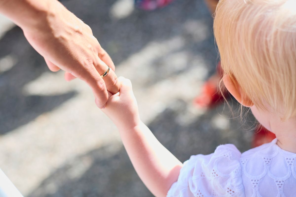 Niña de espaldas agarrada de la mano de un adulto
